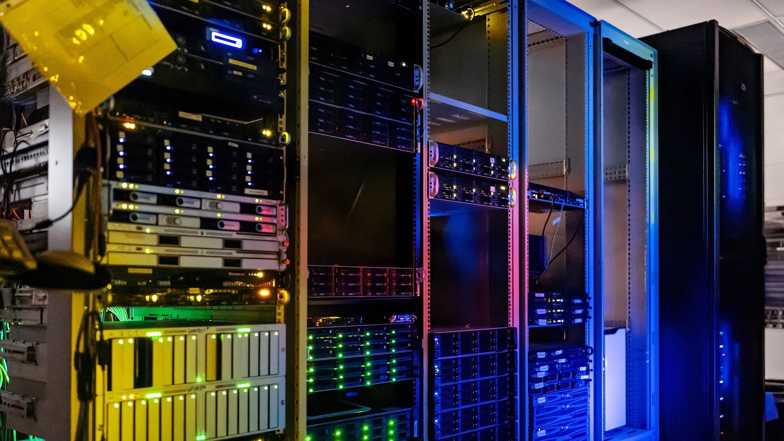 Rows of illuminated server racks in a data centre, cables and drive bays lit in blue and green