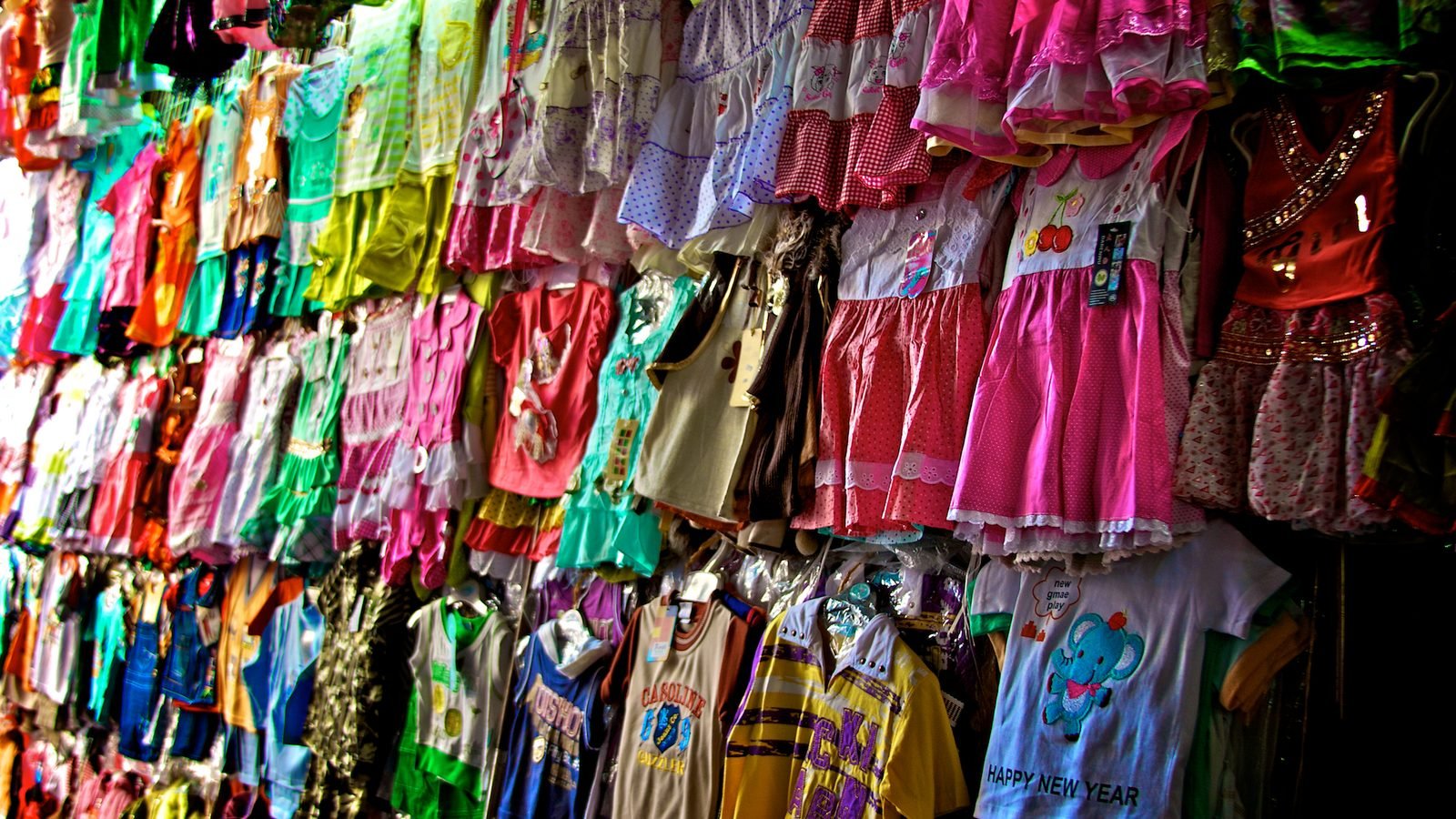 Racks of brightly coloured children's clothes hanging at a stall in the old souks of Dubai