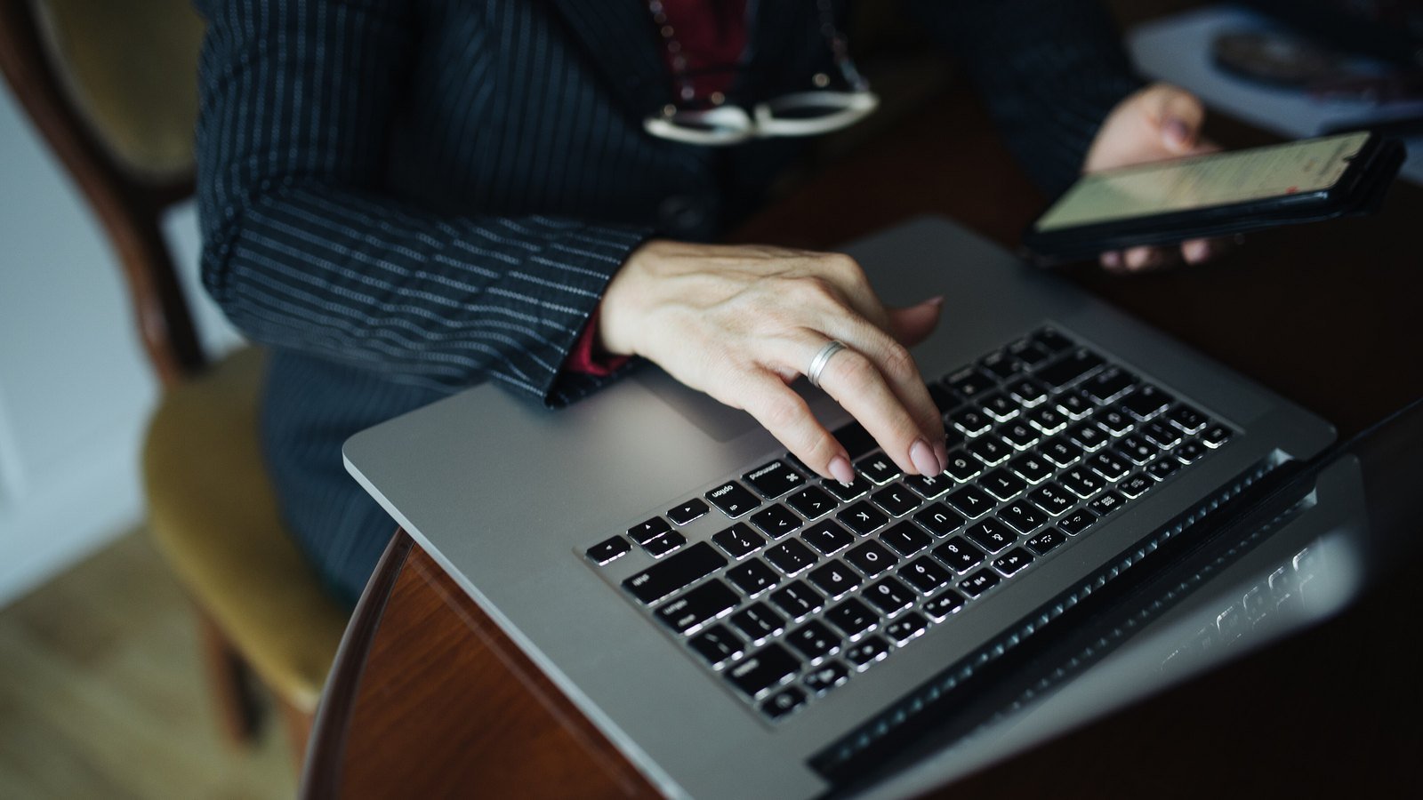 A person typing on a laptop while holding a phone