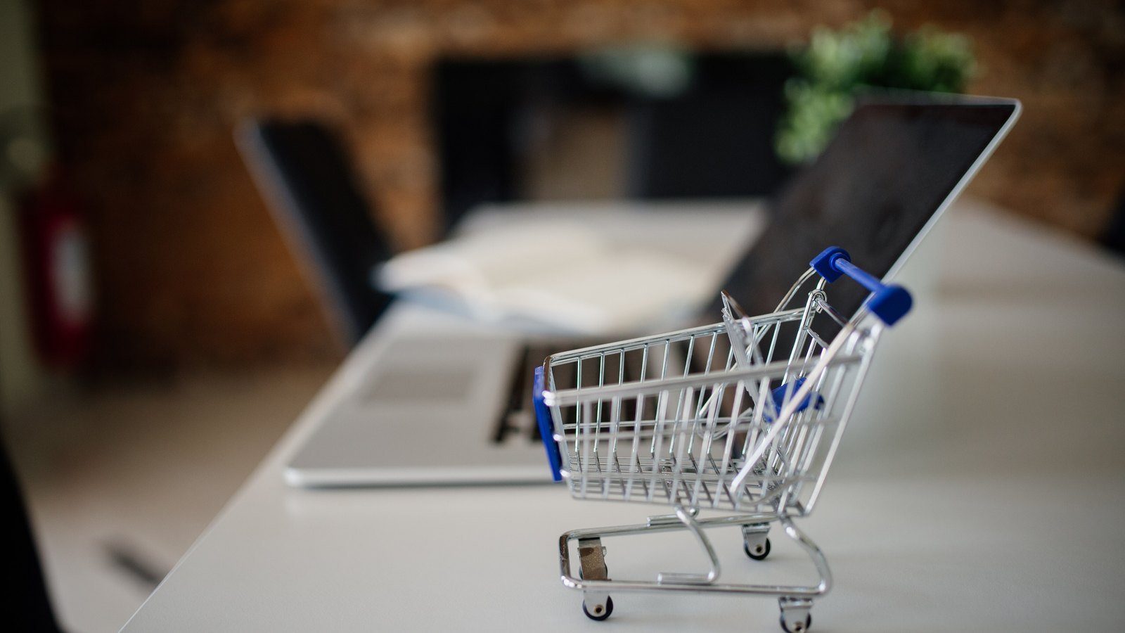 A small shopping cart beside an open laptop on a desk